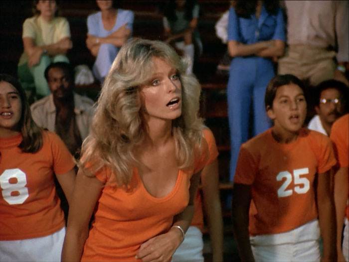 Coach Jill (Farrah Fawcett) in burnt orange t-shirt, surrounded by the kids on her team.